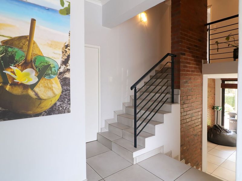 Entrance area featuring a tiled staircase with a modern metal balustrade and an exposed brick feature wall, leading to an open lower level.