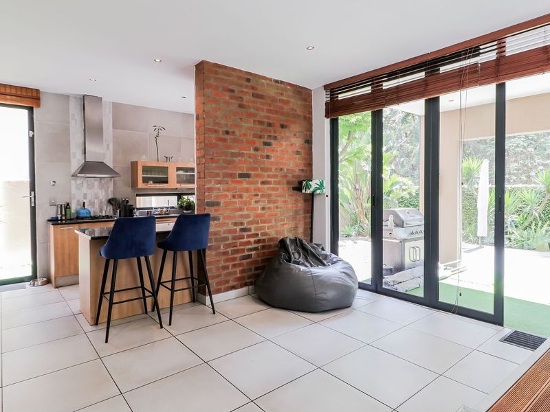 Modern open-plan living and kitchen area featuring an exposed brick wall, tiled floors, and large sliding doors opening to the garden.