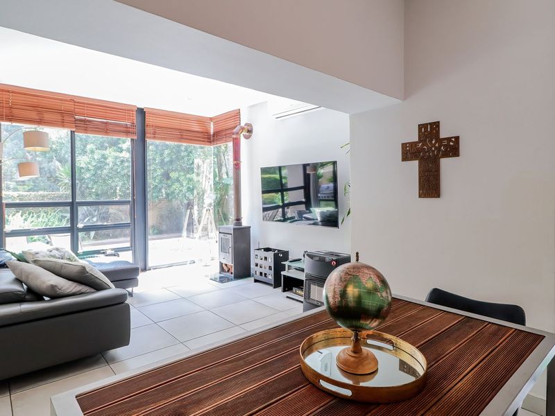 Bright open-plan living area featuring large glass sliding doors, tiled flooring, and a modern freestanding fireplace, creating a seamless connection to the outdoor space.