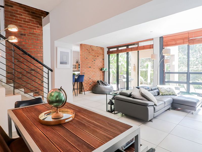 Spacious open-plan living and dining area featuring exposed brickwork, modern tiled floors, and large sliding doors that provide seamless access to the outdoor space.