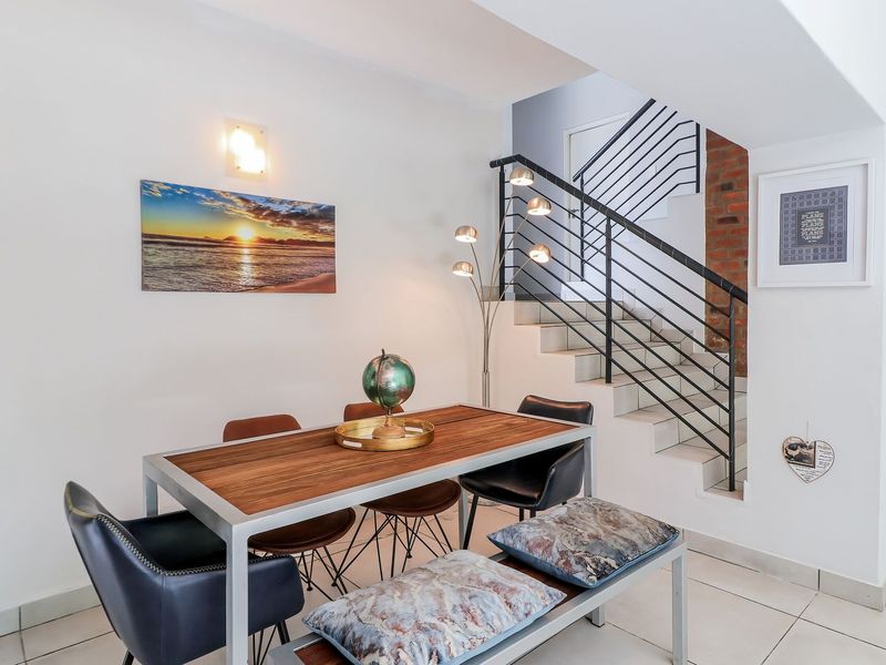 A bright dining area featuring tiled flooring, an exposed brick accent wall, and a modern staircase with a sleek metal balustrade.