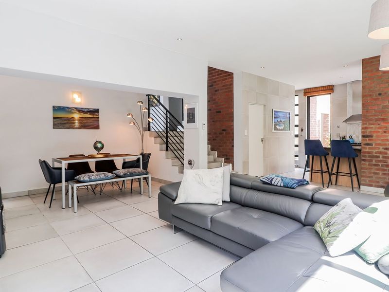 Spacious open-plan living and dining area featuring modern tiled floors, an exposed brick feature wall, and a staircase with a contemporary metal balustrade.