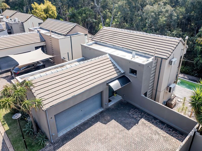 Aerial view of a cluster home featuring a paved driveway, garage, tiled roof, and a private swimming pool in a landscaped setting.