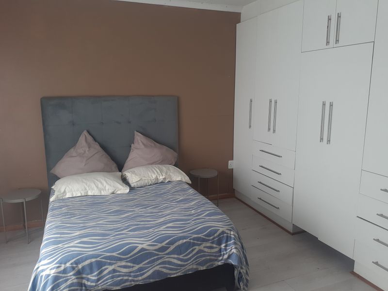 A bedroom featuring white built-in cupboards and light-toned laminate flooring, providing ample storage space.