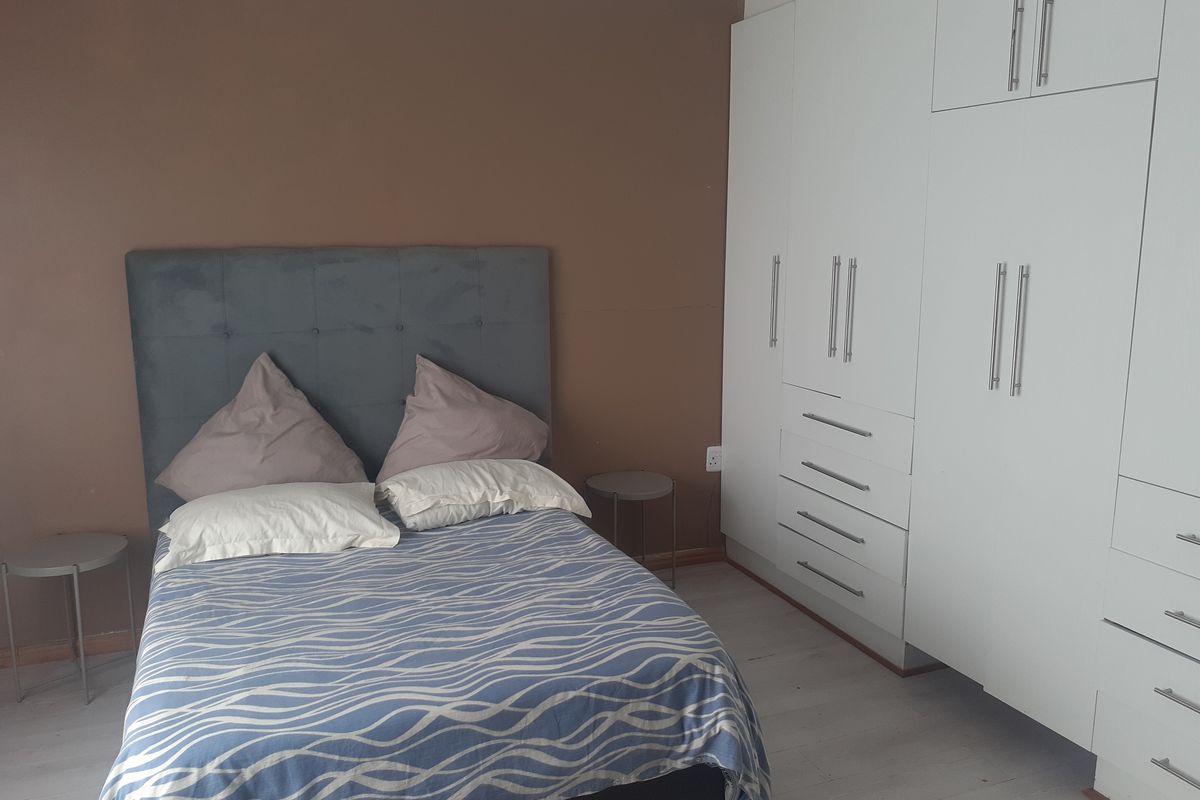A bedroom featuring white built-in cupboards and light-toned laminate flooring, providing ample storage space.