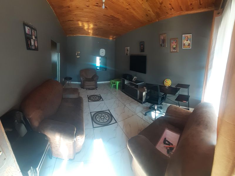 A living room featuring a vaulted timber ceiling and tiled flooring with decorative inlays, providing a functional and comfortable living space.