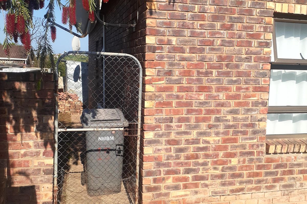 A view of the rear exterior area featuring face brick walls, a chain link gate, and concrete paving.