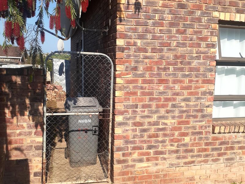 A view of the rear exterior area featuring face brick walls, a chain link gate, and concrete paving.