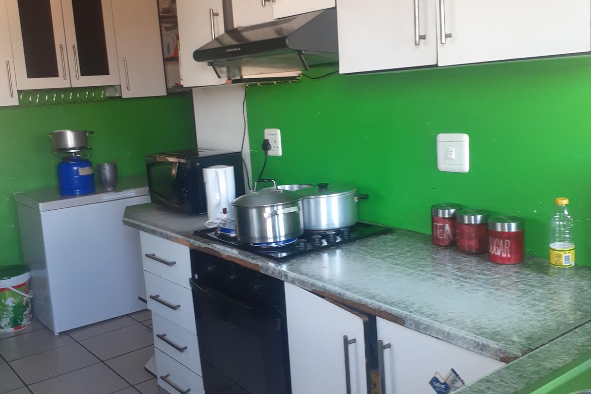 A functional kitchen featuring white cabinetry, laminate countertops, a built-in oven with hob, and an extractor fan, with tiled flooring throughout.