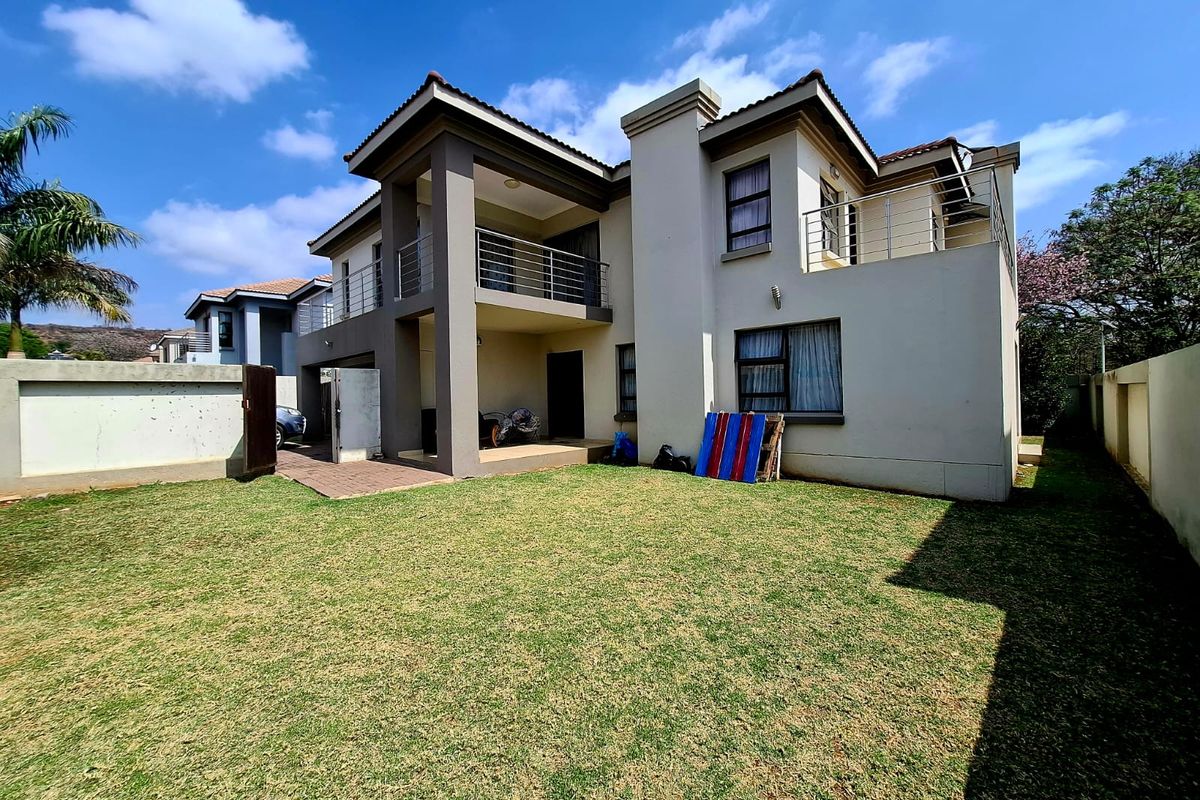 Rear view of a double-story house featuring a paved patio, upper-level balcony with stainless steel balustrades, and a well-maintained lawn.