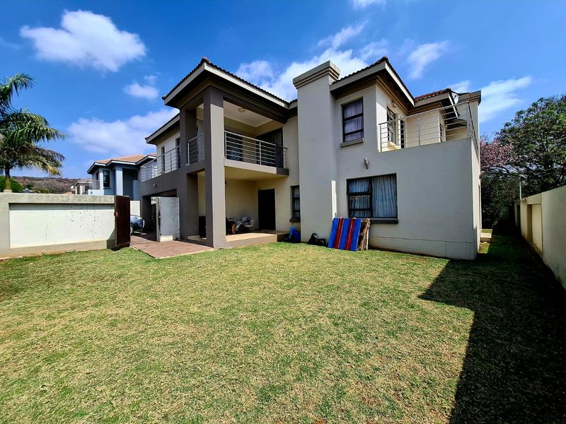 Rear view of a double-story house featuring a paved patio, upper-level balcony with stainless steel balustrades, and a well-maintained lawn.