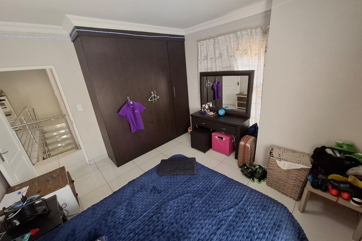 A well-maintained bedroom featuring built-in dark wood cupboards, tiled flooring, and crown molding, with an adjacent view of the staircase.