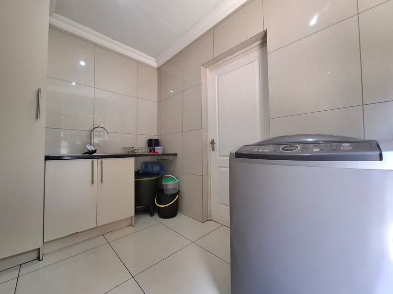 A clean and functional laundry room featuring tiled walls, floor-to-ceiling tiling, built-in cabinetry with a sink, and space for a washing machine.