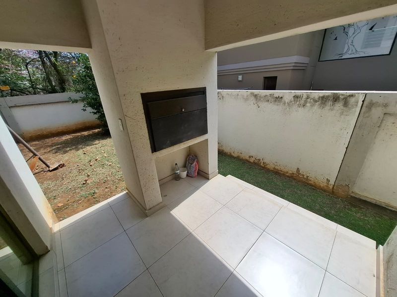 Covered patio area featuring a built-in braai and tiled flooring, overlooking a small garden space with boundary walls.