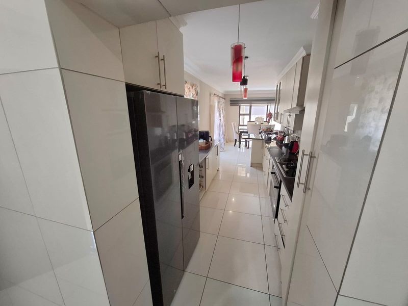 Modern galley-style kitchen featuring high-gloss cabinetry, tiled flooring, and integrated appliances, leading into an open-plan dining area.