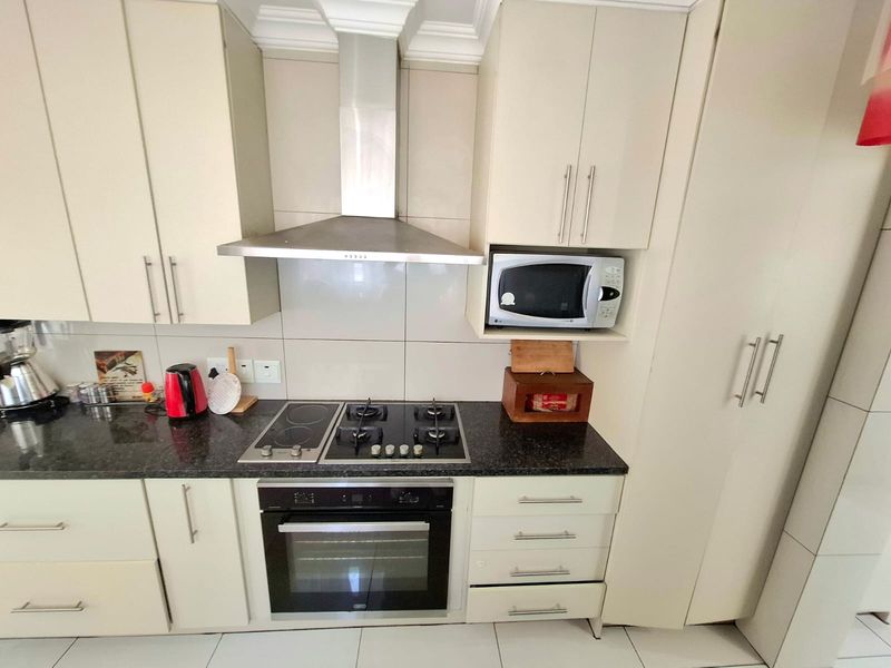 A well-maintained kitchen featuring granite countertops, a combination gas and electric hob, built-in oven, extractor fan, and integrated microwave with ample cabinetry.