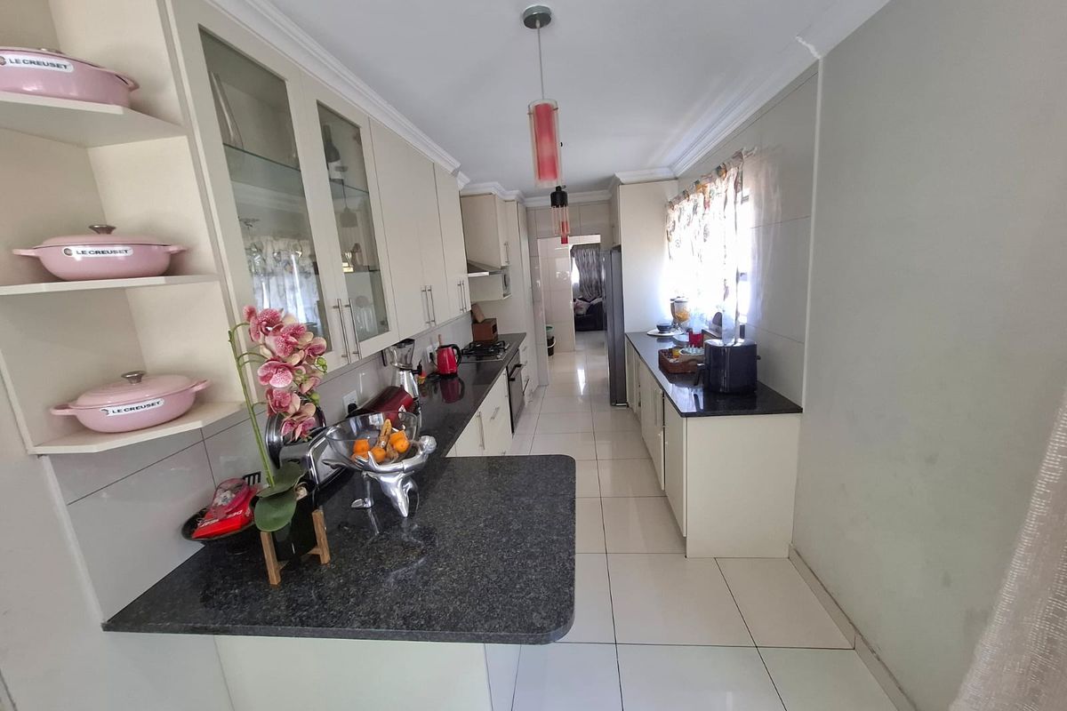 A well-maintained galley-style kitchen featuring granite countertops, ample built-in cabinetry, glass-front display units, and polished ceramic floor tiles.