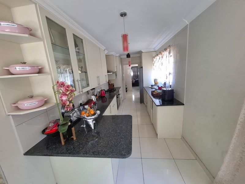 A well-maintained galley-style kitchen featuring granite countertops, ample built-in cabinetry, glass-front display units, and polished ceramic floor tiles.