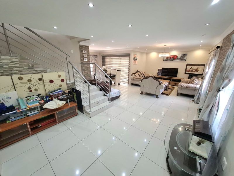 Spacious open-plan living area featuring polished tiled flooring, recessed lighting, and a modern staircase with a stainless steel balustrade.