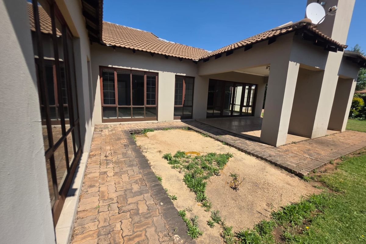 Rear view of the house featuring a covered patio, brick paved courtyard, and large sliding glass doors leading into the living areas.