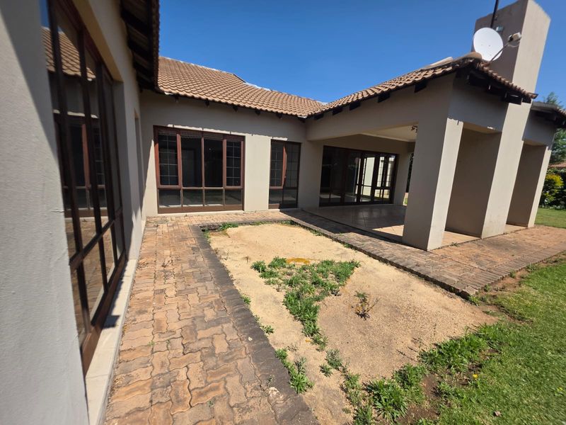 Rear view of the house featuring a covered patio, brick paved courtyard, and large sliding glass doors leading into the living areas.