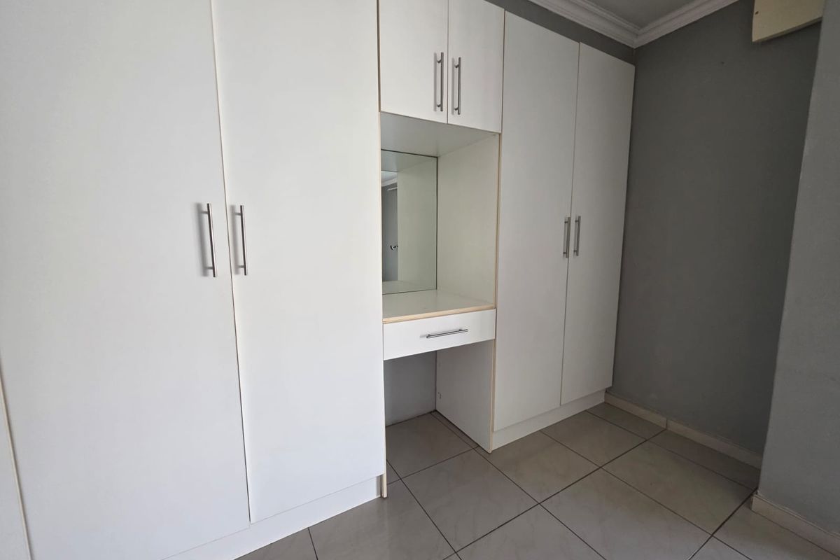 A clean bedroom featuring white built-in cupboards with an integrated vanity station and neutral tiled flooring.