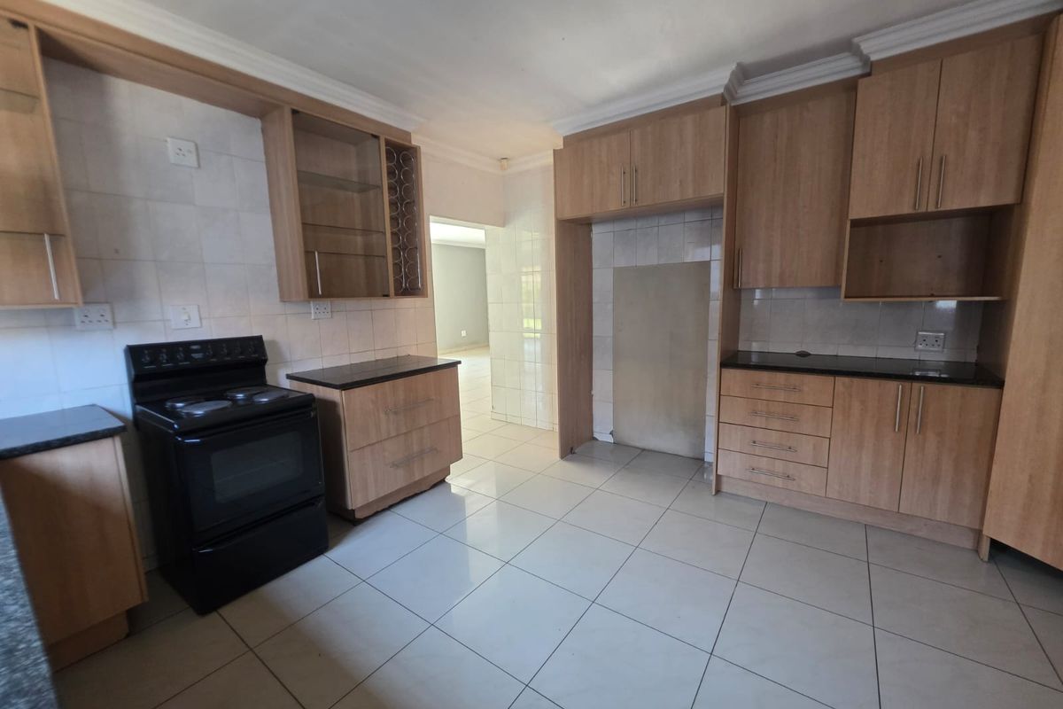 A functional kitchen featuring light wood-tone cabinetry, dark countertops, tiled flooring, and a freestanding stove, offering a clean canvas for potential updates.