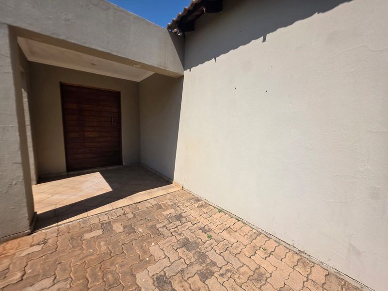 A view of the front entrance featuring a timber door, tiled porch area, and paved driveway with plastered exterior walls.