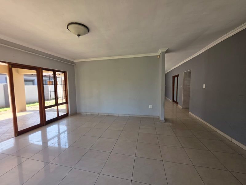 Spacious, empty living area featuring neutral tiled flooring, coved cornicing, and large sliding glass doors providing access to the outdoor patio.