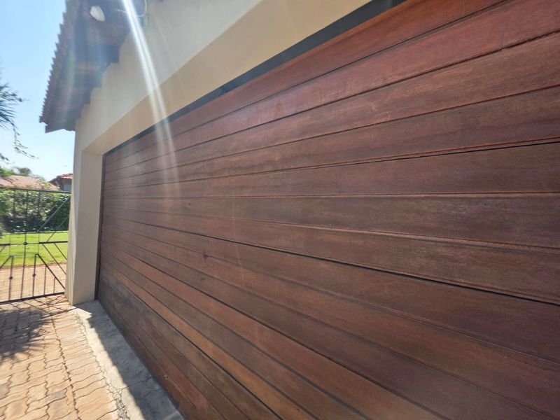 Exterior view of a timber garage door with a paved driveway and metal gate access.