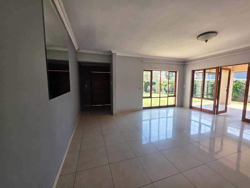 Spacious, light-filled living area featuring neutral tiled flooring, large wooden-framed windows, and direct access to the outdoor patio area.