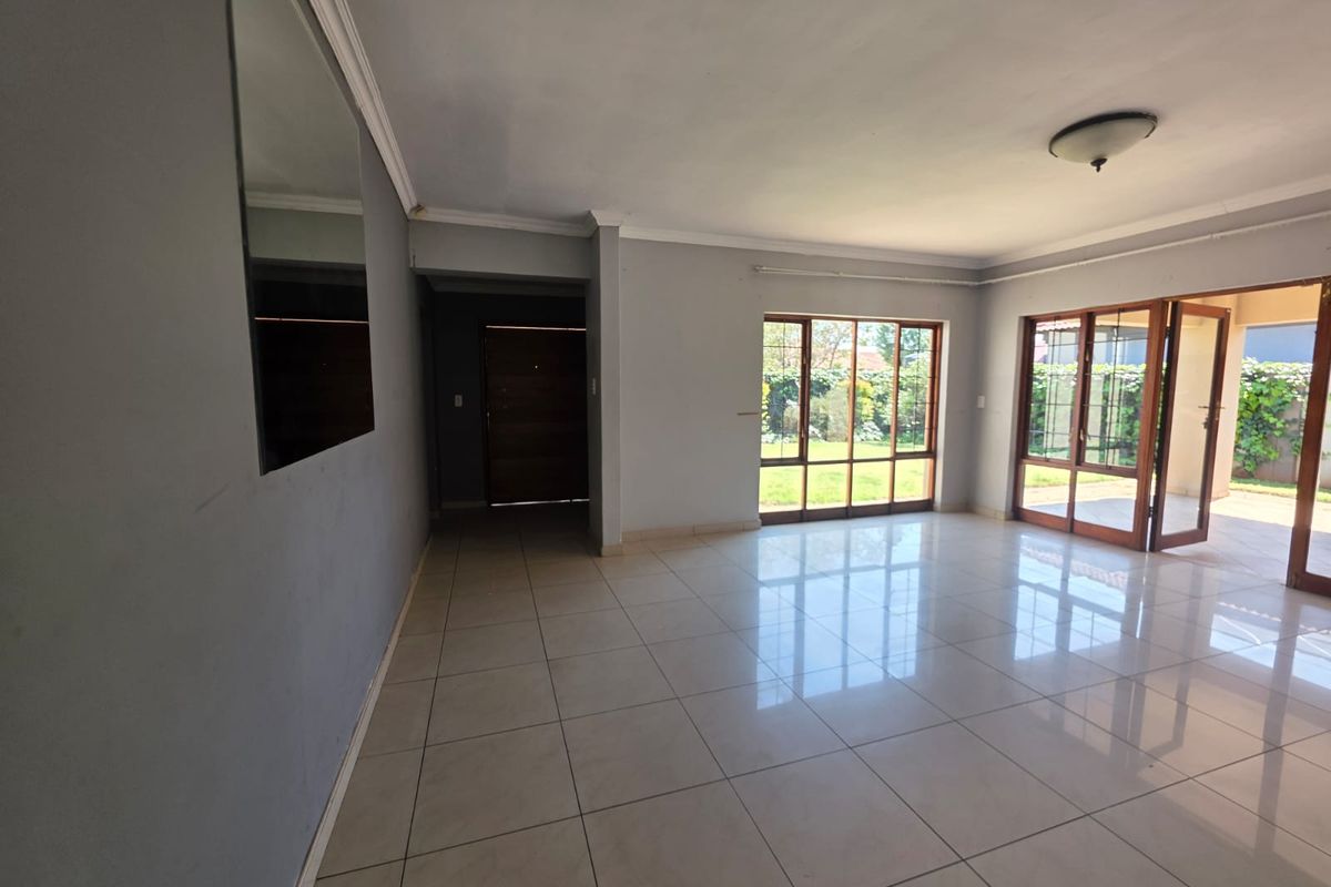 Spacious, light-filled living area featuring neutral tiled flooring, large wooden-framed windows, and direct access to the outdoor patio area.