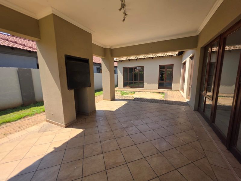 A spacious covered patio featuring a built-in braai, tiled flooring, and direct access to the home through large sliding doors.