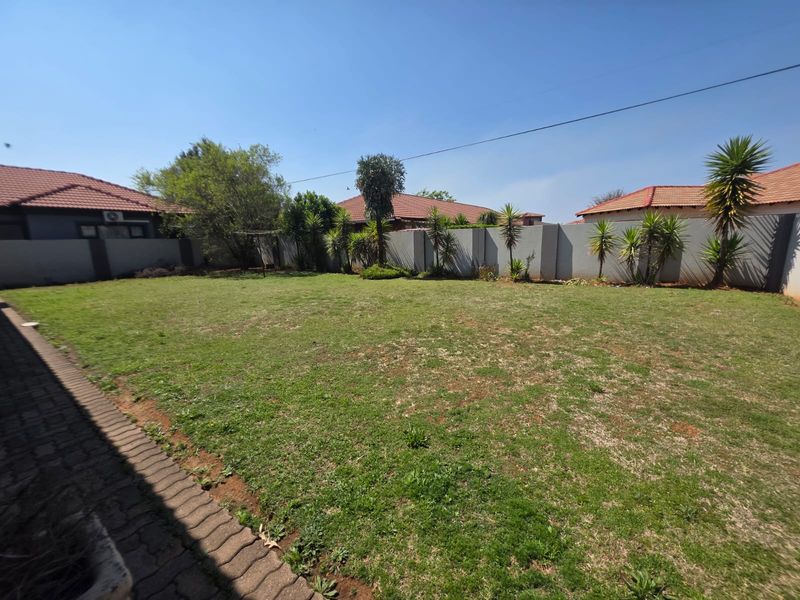 A spacious rear garden featuring a large lawn area, perimeter boundary walls, and a paved walkway along the edge of the property.