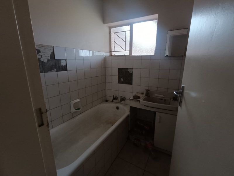 A dated bathroom featuring a bathtub and wall-mounted basin, requiring significant renovation and tile repairs to restore functionality and aesthetic appeal.
