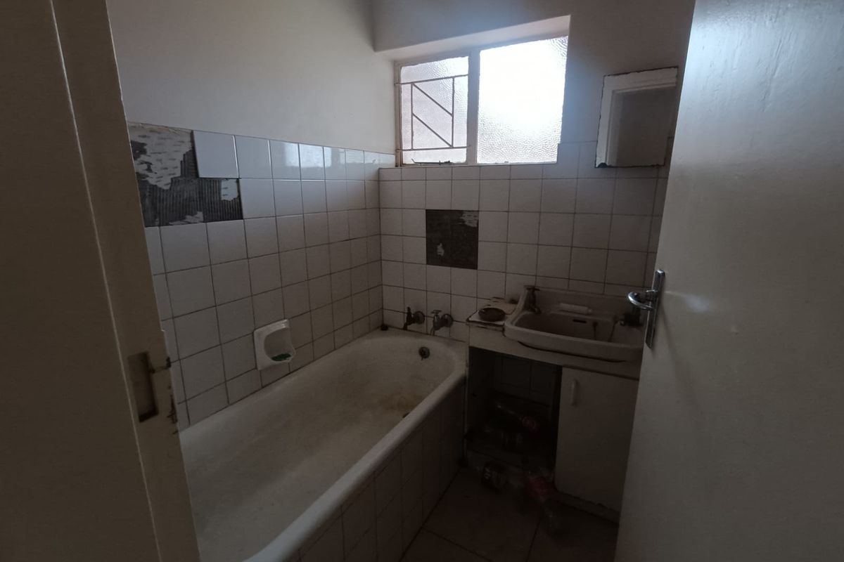 A dated bathroom featuring a bathtub and wall-mounted basin, requiring significant renovation and tile repairs to restore functionality and aesthetic appeal.