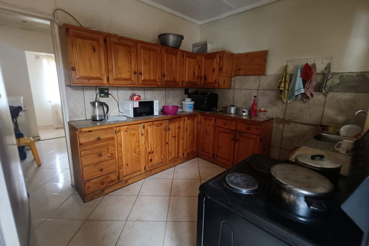 A functional kitchen featuring wooden cabinetry, tiled backsplash, and tiled flooring, currently showing signs of wear and requiring cosmetic updates.