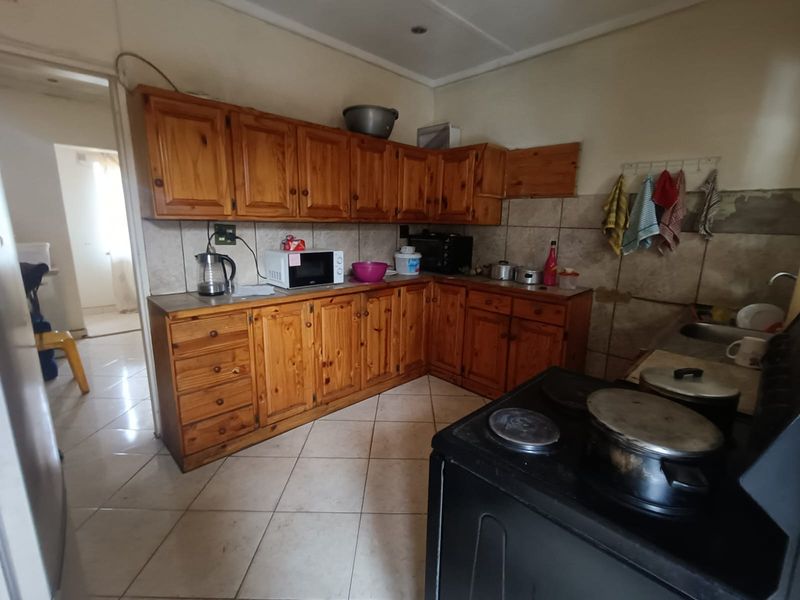 A functional kitchen featuring wooden cabinetry, tiled backsplash, and tiled flooring, currently showing signs of wear and requiring cosmetic updates.
