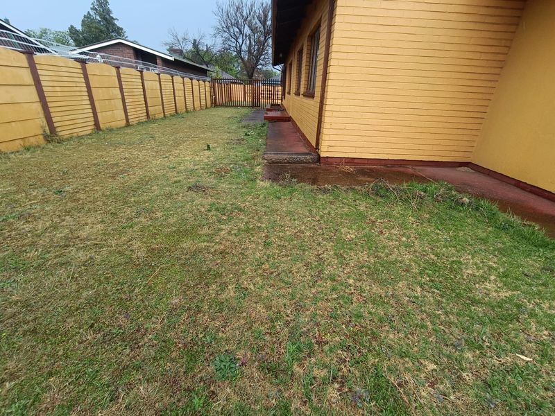 A view of the rear garden area featuring a brick boundary wall, a concrete pathway along the house, and a metal security gate.