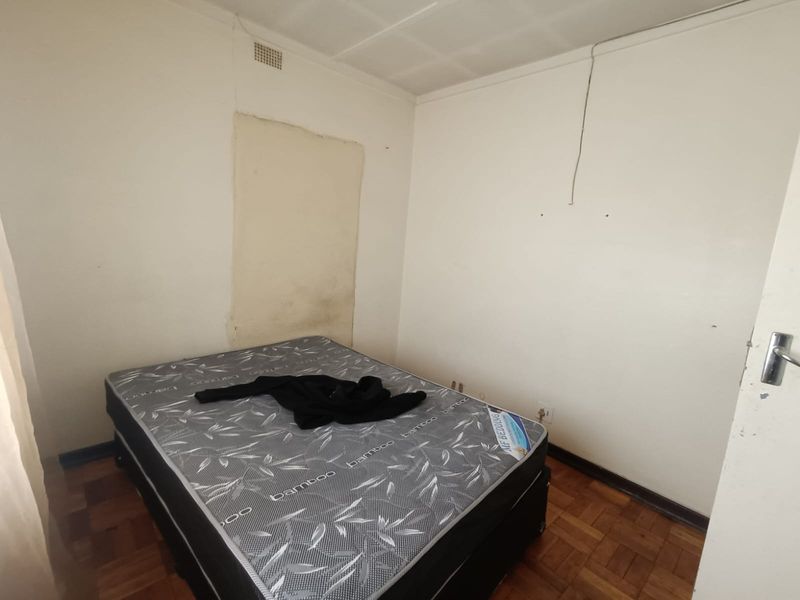 A bedroom featuring parquet flooring and a ceiling vent, currently requiring cosmetic updates to the wall finishes and general maintenance.
