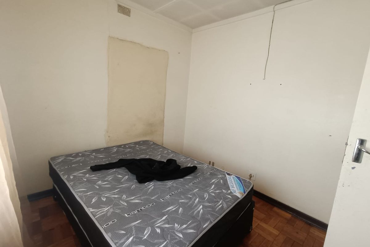 A bedroom featuring parquet flooring and a ceiling vent, currently requiring cosmetic updates to the wall finishes and general maintenance.