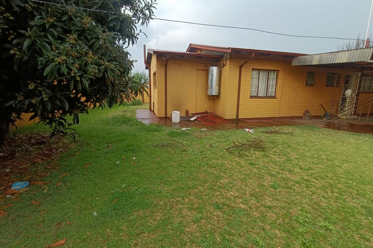 Rear view of a single-story brick house featuring a lawn, concrete patio area, and external geyser installation.