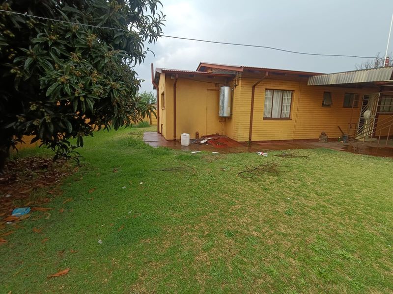 Rear view of a single-story brick house featuring a lawn, concrete patio area, and external geyser installation.