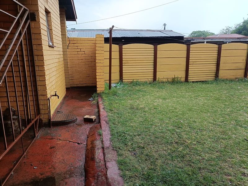A view of the rear exterior area featuring a brick wall, precast boundary fencing, and a concrete pathway with an outdoor water tap.