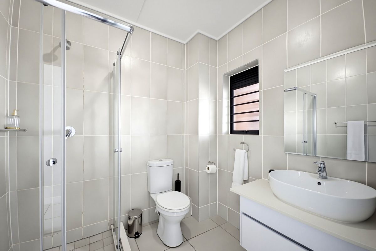 Modern bathroom featuring a glass-enclosed shower, a sleek vanity with a countertop basin, and neutral floor-to-ceiling wall tiles.