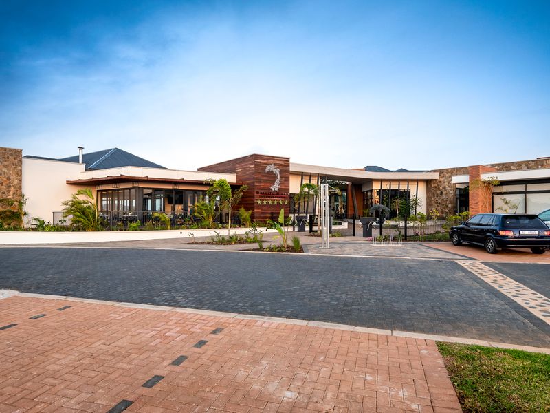 Modern apartment complex entrance featuring stone and timber facade with paved driveway and landscaped surroundings.