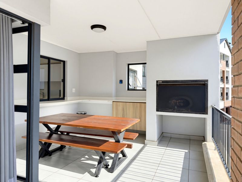 A covered balcony featuring a built-in braai, tiled flooring, and a convenient prep area with cabinetry and stone countertops, ideal for outdoor dining.