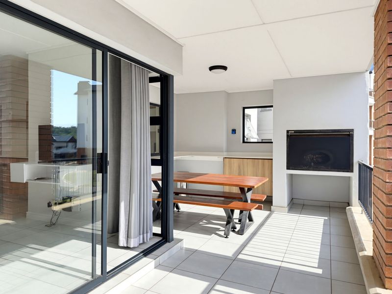 Covered balcony featuring a built-in braai, tiled flooring, and direct access to the interior through large sliding glass doors.