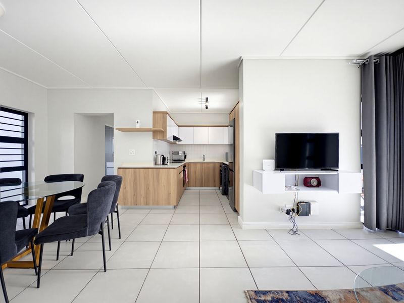 Modern open-plan living and kitchen area featuring light wood cabinetry, tiled flooring, and a sleek floating media console in a well-maintained apartment.
