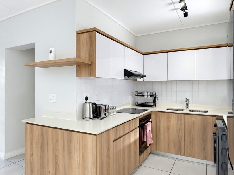 Modern kitchen featuring sleek wood-grain and white cabinetry, stone countertops, integrated appliances, and a clean tiled backsplash.